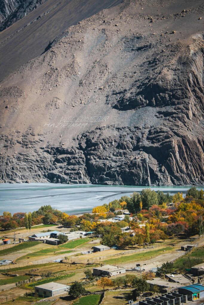A picturesque view of Abbottabad featuring a lake, village, and mountain backdrop in autumn.