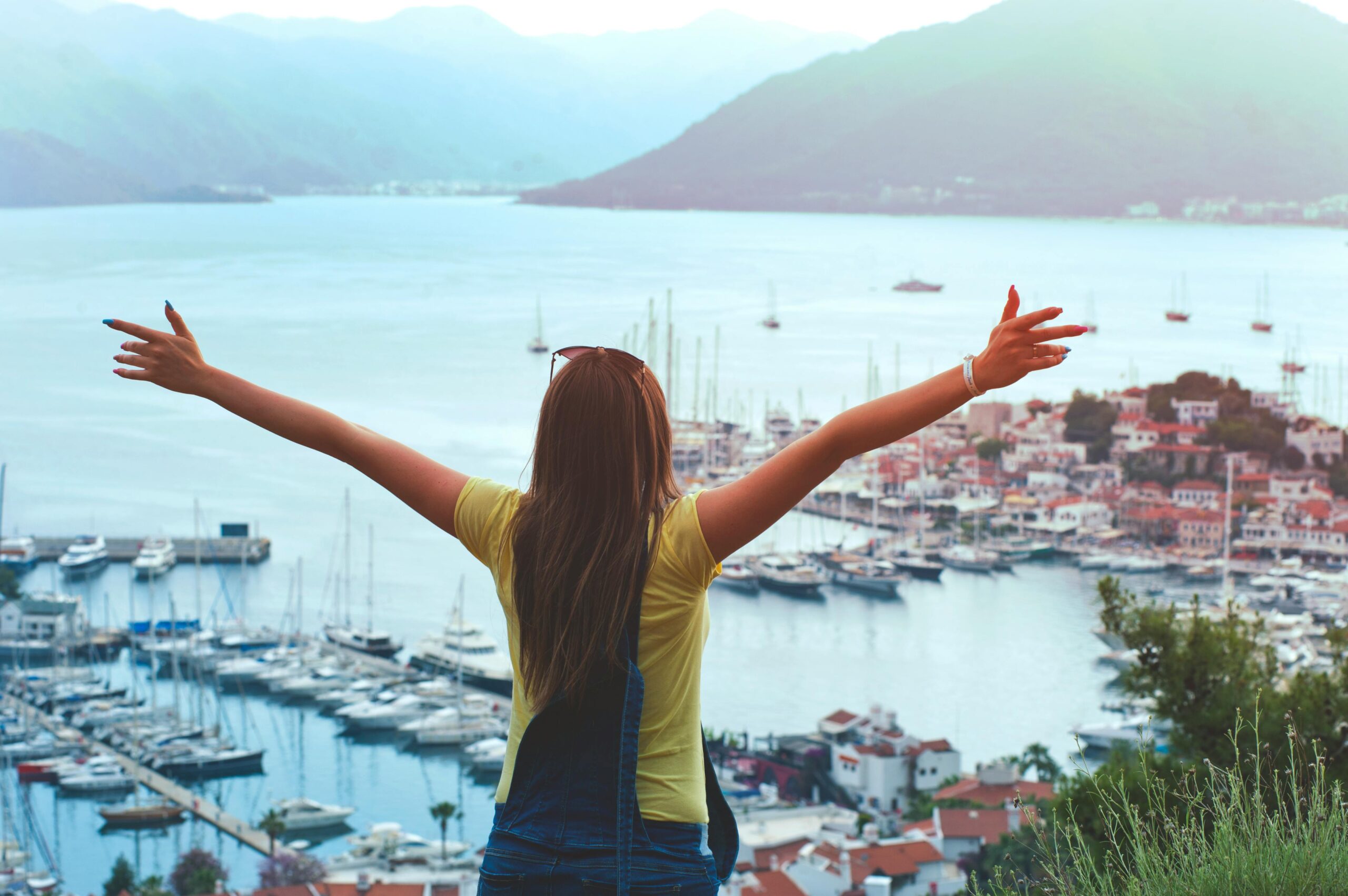 A woman with open arms enjoys a scenic summer view of Marmaris harbor and yachts.